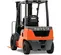 Rear view of orange and black Toyota warehouse forklift with black lifting mast and orange forks with an open cabin.