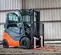 Front angled view of orange and grey Toyota warehouse forklift with a mast, orange forks and enclosed cabin in a warehouse.