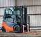 Front angled view of orange and grey Toyota warehouse forklift with a mast, orange forks and enclosed cabin in a warehouse.