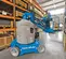 Side view of a blue Genie vertical mast boom lift with an operator using lift in warehouse aisle.