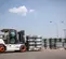 A white and black Bobcat D70 forklift with orange wheel hubs is shown from its left side, slightly from the front, lifting a pallet of shrink-wrapped tires. The forklift is in an outdoor industrial area with rows of stacked, shrink-wrapped tires in the background, under a blue sky with scattered clouds.