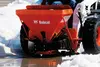 Red Bobcat Spreader Attachment on a skid steer in the snow